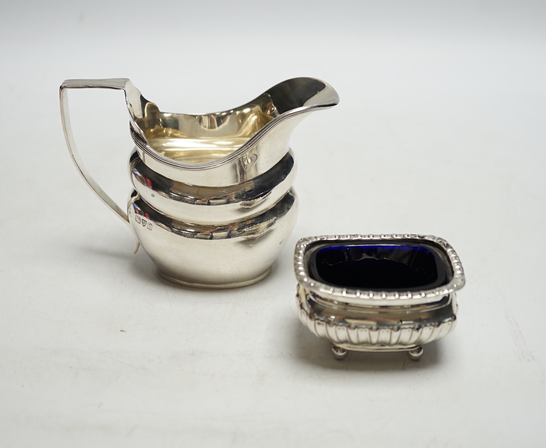 A George V silver helmet shaped cream jug and a silver salt with a gadrooned border.